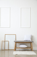 Comfortable bench with pillows and frames near light wall