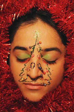 closeup portrait of young woman with christmas tree decorations with piercing on face for 2022 new year celebration