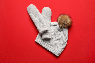 Warm mittens and hat on red background