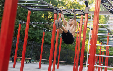 Athletic male athlete with a naked torso trains the abdominal muscles by lifting his legs up on...
