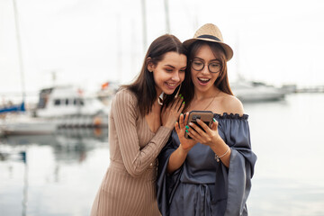 Two surprised cute women friend look at the smartphone screen in the yacht club