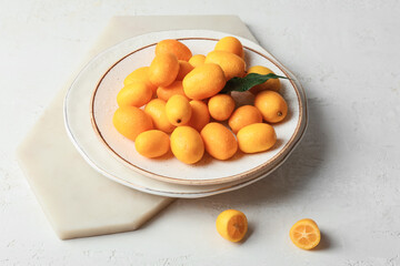 Plate with tasty kumquat fruits on light background