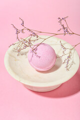 Bowl with bath bomb and dried flower on pink background, closeup