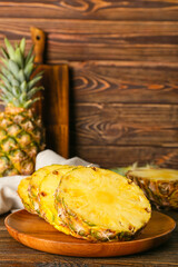 Plate with pieces of ripe juicy pineapple on wooden background