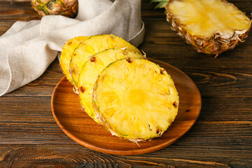 Plate with pieces of ripe juicy pineapple on wooden background