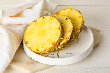 Plate with pieces of ripe juicy pineapple on light wooden background