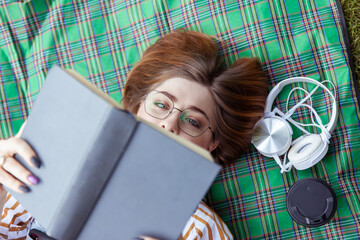 Obraz premium Young woman student reads a book while lying on a blanket in the park