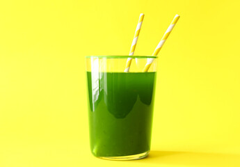 Glass of green juice with straws on yellow background