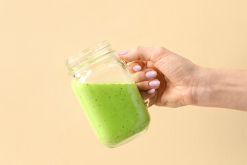 Woman holding mason jar of green juice on beige background