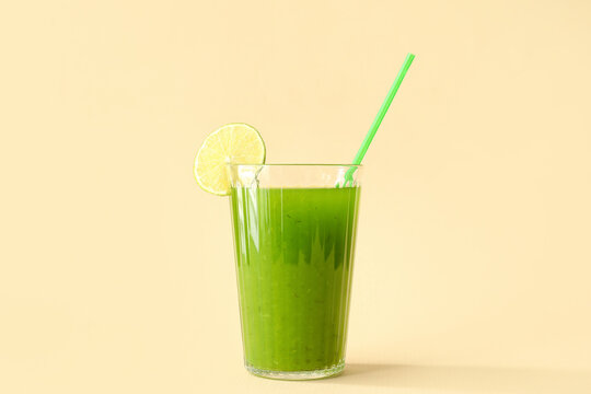 Glass of green juice with straw and lime slice on beige background