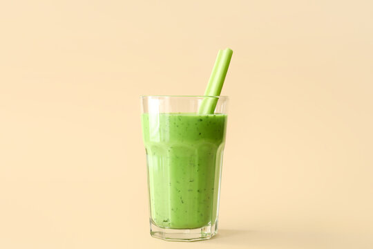 Glass of green juice with celery on beige background