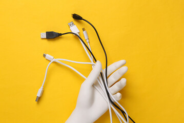 White plastic hand holding Different usb cables on yellow background. Top view