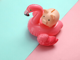 Summer vacation concept. Piggy bank on inflatable flamingo, pink blue background