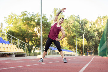 Obraz premium Athletic muscular man warming up before running in stadium. Healthy lifestyle