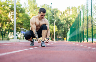 Athletic man tying the laces of sneakers at the stadium