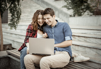 Young cheerful couple of lovers spend time together while use laptop outdoors. Happy, funny people. Love concept.