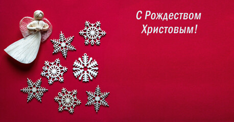 Greeting card for Orthodox Christmas. White wooden snowflakes and an angel on a red background. Text in the Russian language means Merry Christmas! 
