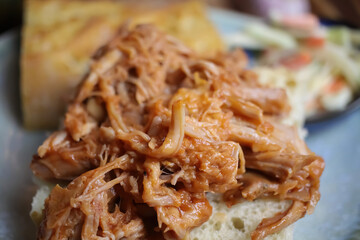 Closeup of dish with marinated pulled pork on fresh baguette, blurred cole slaw salad background