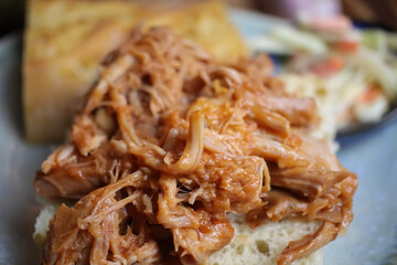 Closeup of dish with marinated pulled pork on fresh baguette, blurred cole slaw salad background