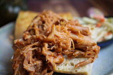 Closeup of dish with marinated pulled pork on fresh baguette, blurred cole slaw salad background