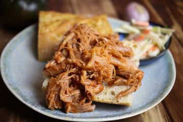 Closeup of dish with marinated pulled pork on fresh baguette, blurred cole slaw salad background