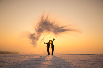 Young man and woman in love make fun in cold winter morning with hot water who freezes in the cold air. Valentine photo with space for your montage