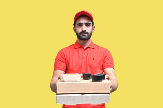 delivery man in red t shirt and cap front look holding 2 packaging box indian pakistani model