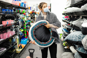 Attractive young woman in mask and plaid scarf holds dog bed in animal department of shopping mall.Concept of shopping for home.New normal concept.Protection medical mask.