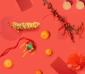 Abstract concept of Chinese new year celebration. Tiger toy, oranges, branch with red berries, red cards and two cups of tea, colorful embroidery ball. Flat lay arrangement with red background.
