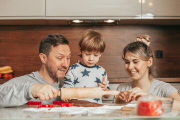 Obraz na płótnie Canvas Parents laugh, happy to spend time with family. Dad, mom and baby. Little son, boy 4 years old before preparing cookies, roll out dough for baking