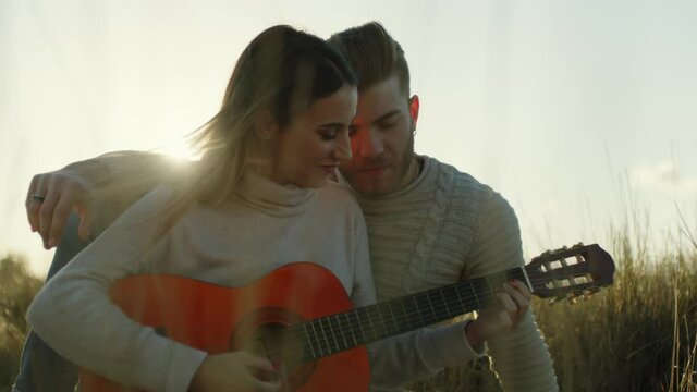 Coppia ragazzo e ragazza suonano la chitarra seduti su un tappeto in campagna al tramonto per san valentino