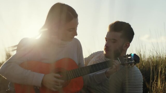 Coppia ragazzo e ragazza suonano la chitarra seduti su un tappeto in campagna al tramonto per san valentino