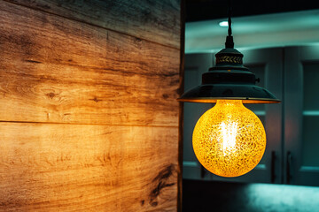 A large yellow light bulb on the background of a wooden wall. Cozy lighting of the kitchen space....
