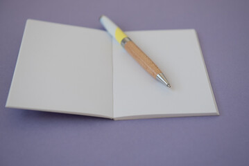 Petit carnet ouvert sur une page blanche avec un stylo - espace vide pour écrire - fond mauve