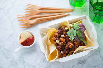 Mince and bean chips in a carton takeaway container, elevated view on a light-grey marble background