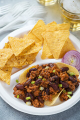 Close-up of nachos chips with minced meat and beans served on a white takeaway plate, vertical shot