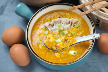 Middle close-up of chinese traditional egg-drop soup with dumpling in a turquoise serving bowl, studio shot on a grey concrete surface