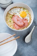 Gong Zai Mein or Hong Kong traditional breakfast served in a white bowl, vertical shot on a light-blue stone background, elevated view