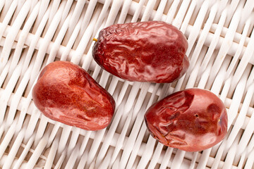 Three sweet dried ziziphus berries on a vine mat, close-up, top view.