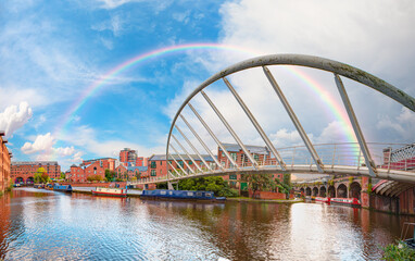 Fototapeta na wymiar Amazing rainbow over the waterway canal area with a narrowboat on the foreground modern bridge, Castlefield district - Manchester, UK
