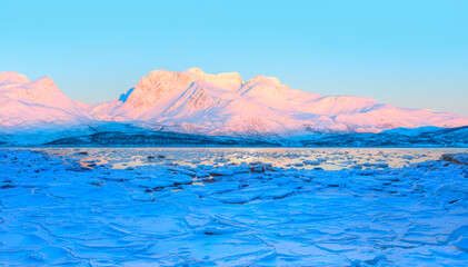 Fototapeta na wymiar Panoramic view at fjord with coast of the Norwegian Sea in the background snowy mountains Arctic Circle at sunset - As a result of melting snow, freezing of the water mixed with the sea -Norway