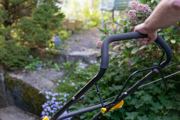 Fototapeta na wymiar Hands of man pushing lawnmower through small backyard in spring. Close-up.