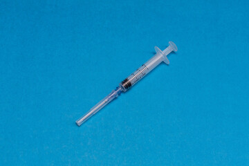 A disposable syringe for injection and white round tablets on a blue background.