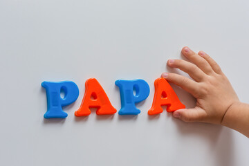 The word PAPA is made of colored magnetic letters typed by a child's hand. Early development of the child.