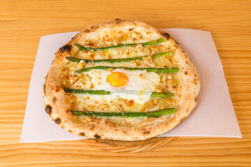 Pizza with wild asparagus, chopped walnuts and fried egg in the center with mozzarella cheese