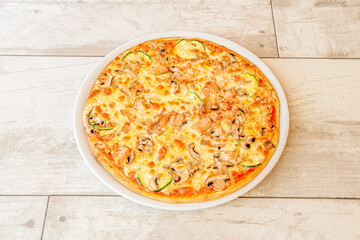 Family pizza with chicken, zucchini slices, mushroom slices and melted cheese on white plate