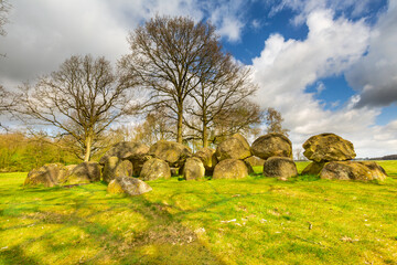 Dolmen D14 in the province of Drenthe in the Netherlands with a background of oak trees and a beautiful Dutch cloudy sky with blue spots. A dolmen is construction work from the new stone age