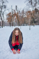 Fototapeta na wymiar a young happy woman is having fun in a winter park, throwing snow, it is cold in her hands, the emissions are off scale.