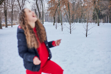 Fototapeta na wymiar a young happy woman is having fun in a winter park, throwing snow, it is cold in her hands, the emissions are off scale.