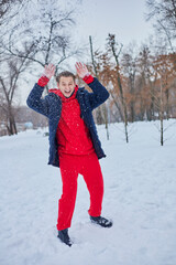 Fototapeta na wymiar a young happy man is having fun in a winter park, throwing snow, it is cold in his hands, the emissions are off scale.